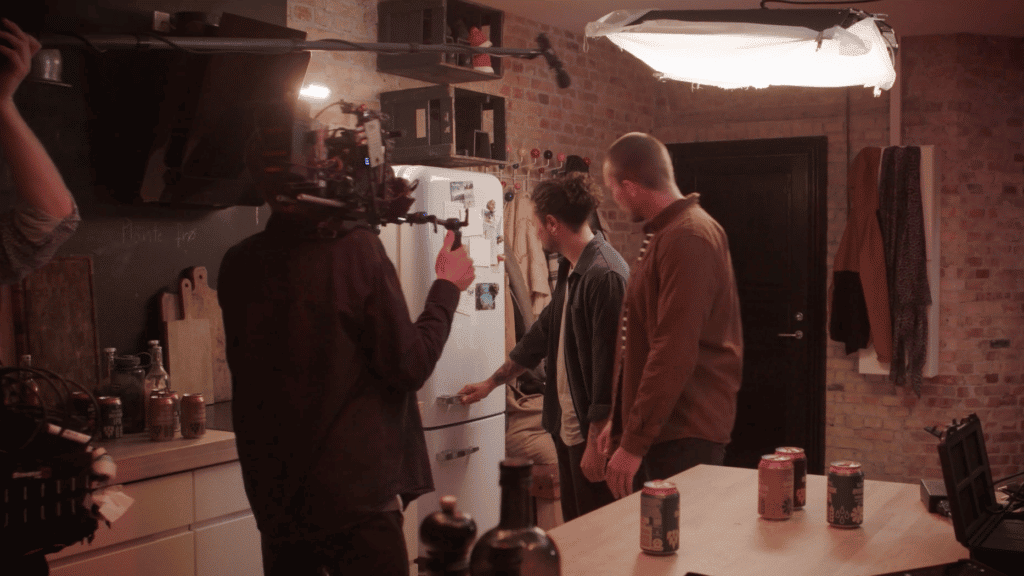 Køkkenkulisse med to personer foran et køleskab. Kameracrew filmer dem.