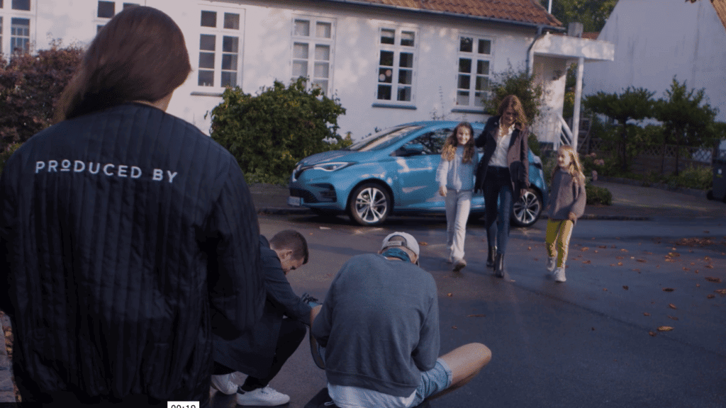 Kvinde med to børn kommer gående fra blå bil. Kameracrew i forgrunden filmer dem.